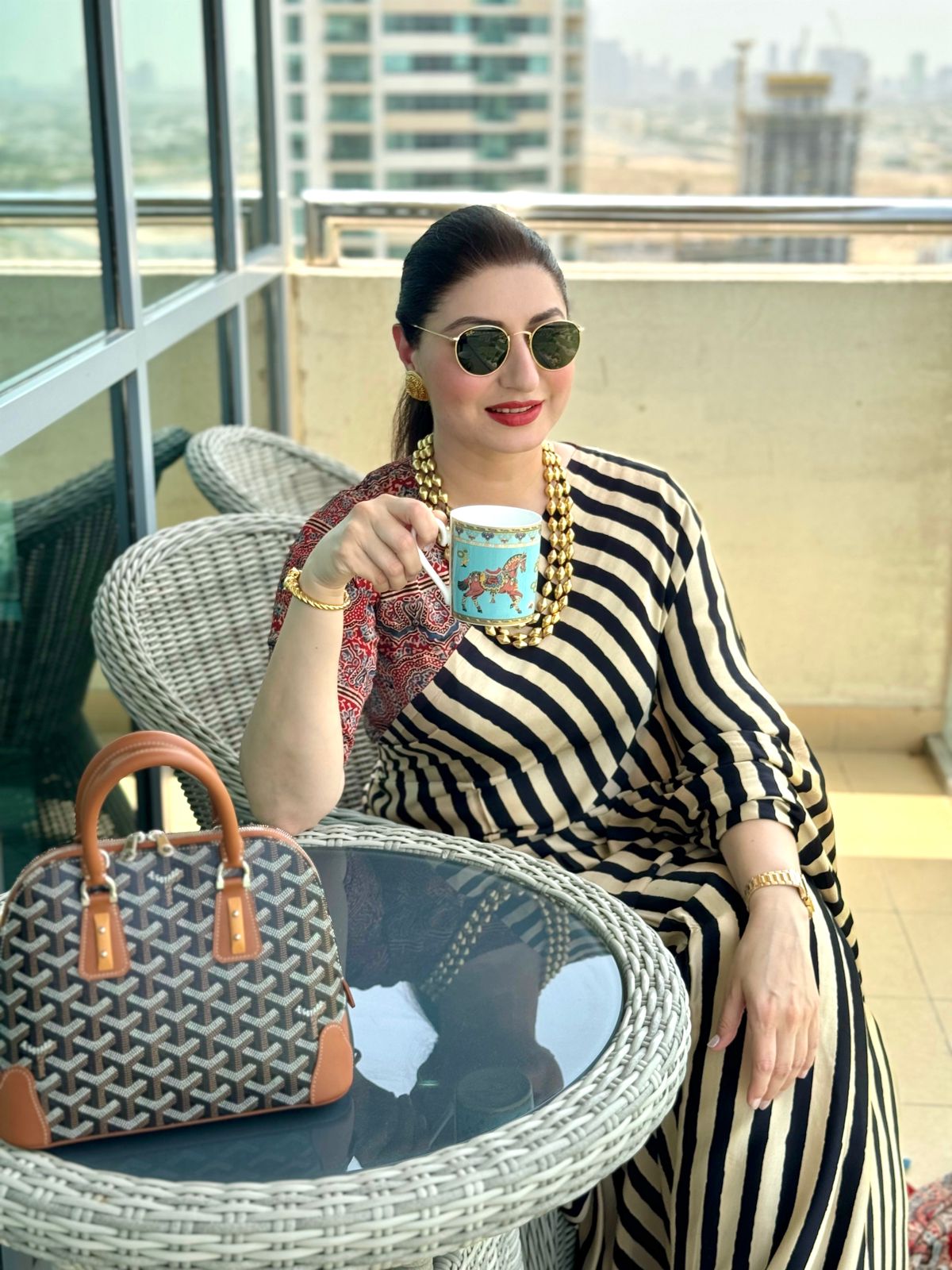 Woman wearing black and beige striped ajrakh saree sitting outdoors with a designer handbag and holding a cup